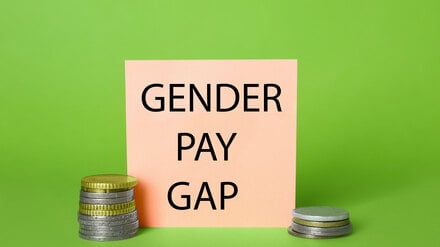 Gender pay gap. Paper note and stacked coins on light green background