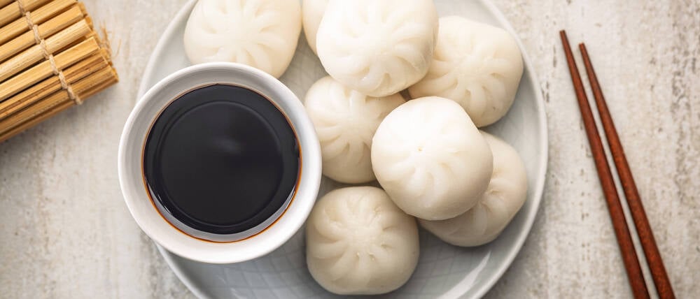 Xiao Long Bao. Chinesische Teigtaschen auf dem Teller und Sojasauce auf dem Küchentisch. Xiao Long Bao.