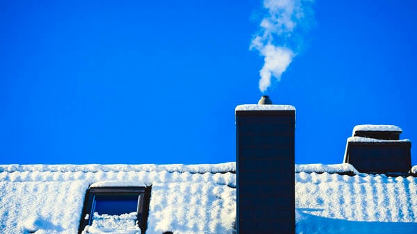 Rauchender Schornstein eines Wohnhauses im Winter (Symbolbild)