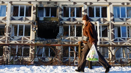 Eine Passantin in Kyjiw vor einer beschädigten Hausfassade.