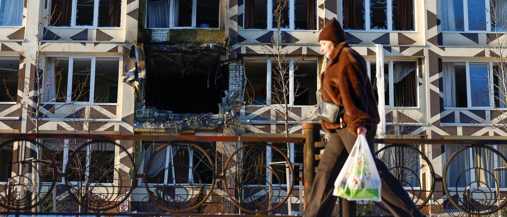 Eine Passantin in Kyjiw vor einer beschädigten Hausfassade.