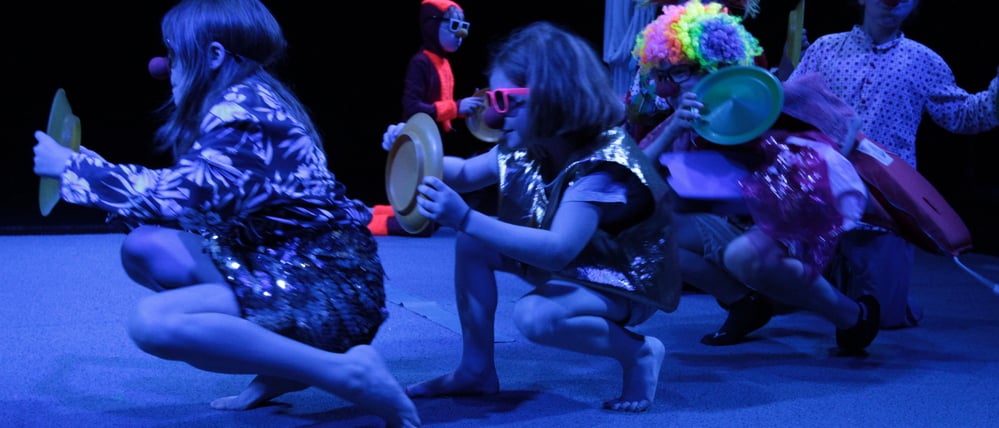 Fünf Kinder bewegen sich in der Hocke vorwärts. Die Kinder sind bunt verkleidet.