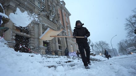 Ein Mann vor dem Landgericht Hamburg räumt den Schnee weg.