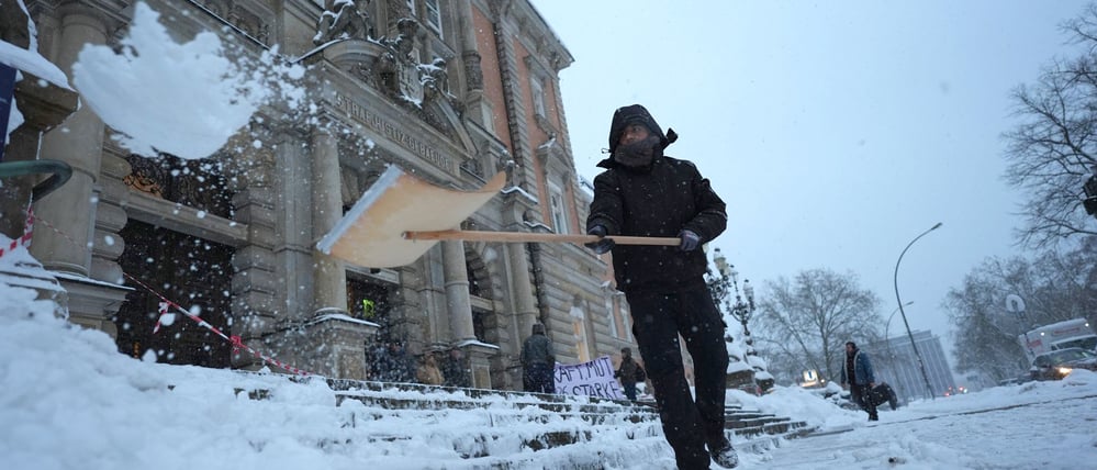 Ein Mann vor dem Landgericht Hamburg räumt den Schnee weg.