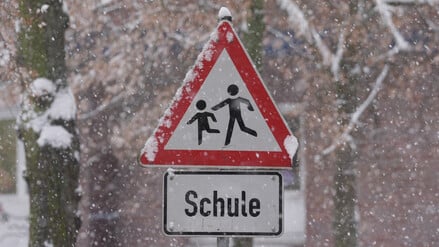 Schnee liegt auf einem Verkehrsschild und Hinweisschild mit der Aufschrift „Schule“ vor einer Schule im Stadtteil St. Georg in Hamburg.