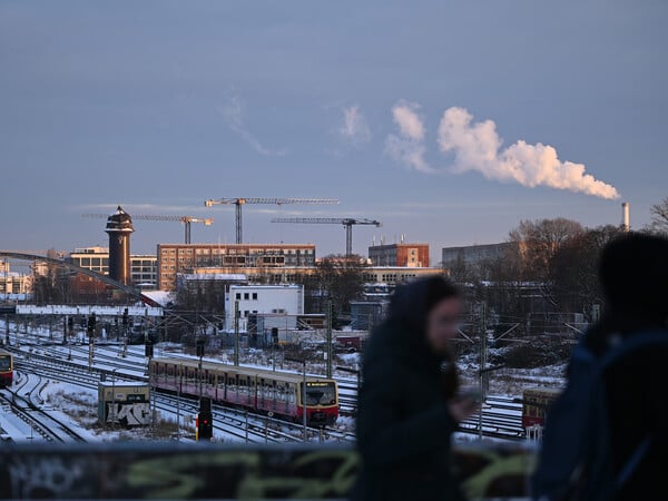 Eine Frau schaut an der S-Bahn-Station Warschauer Straße auf ihr Telefon. Im Hintergrund fährt eine S-Bahn über schneebedeckte Gleise. +++ dpa-Bildfunk +++