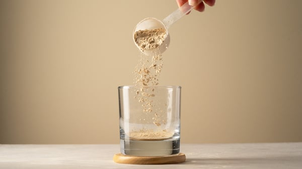Eine Person füllt mit einem Löffel Proteinpulver in ein Glas.