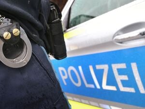 Ein Polizist mit Handschellen und einer Pistole am Gürtel steht vor einem Streifenwagen (Symbolbild).