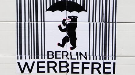 Ein Logo des Volksbegehrens „Berlin Werbefrei“ mit einem Strichcode und einem Berliner Bären mit Regenschirm.
