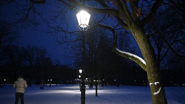Ein Mann geht im Berliner Volkspark Friedrichshain einen beleuchteten Weg entlang.