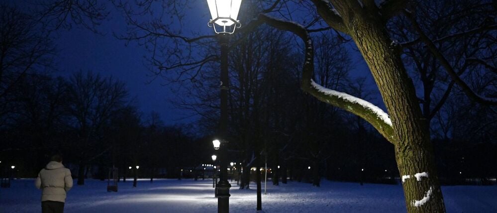 Ein Mann geht im Berliner Volkspark Friedrichshain einen beleuchteten Weg entlang.