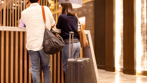 Ein Paar mit Koffer an einer Hotelrezeption (Symbolbild)