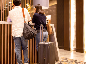 Ein Paar mit Koffer an einer Hotelrezeption (Symbolbild)