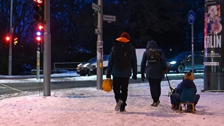Eine Familie zieht einen Schlitten auf dem verschneiten Gehweg in Berlin Mitte. 