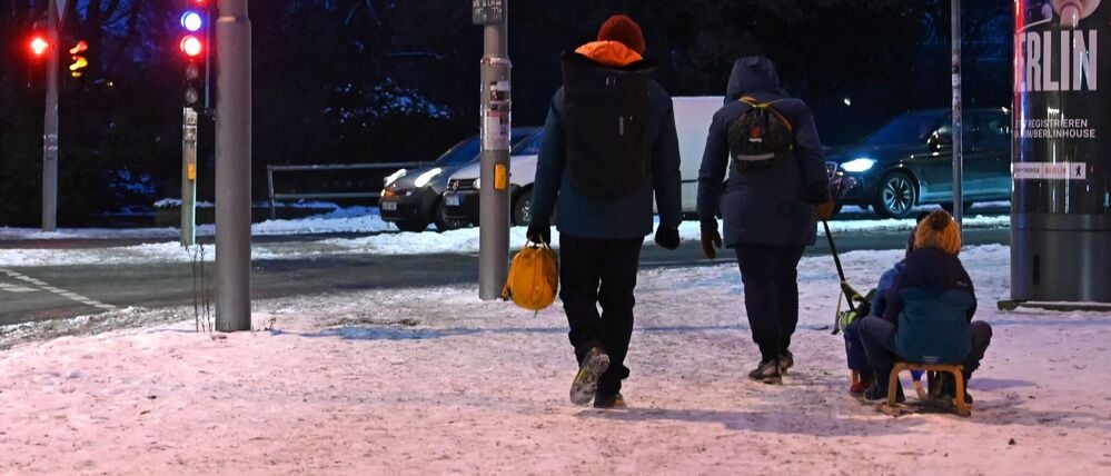 Eine Familie zieht einen Schlitten auf dem verschneiten Gehweg in Berlin Mitte. 