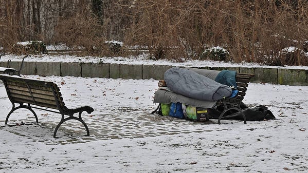 Eine obdachlose Person liegt in einem Schlafsack auf einer Parkbank. (Symbolbild)