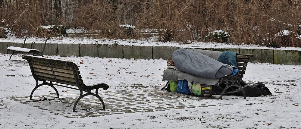 Eine obdachlose Person liegt in einem Schlafsack auf einer Parkbank. (Symbolbild)