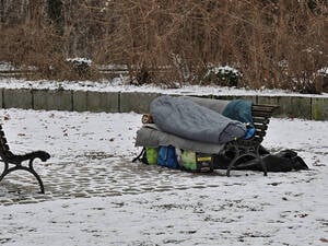Eine obdachlose Person liegt in einem Schlafsack auf einer Parkbank. (Symbolbild)
