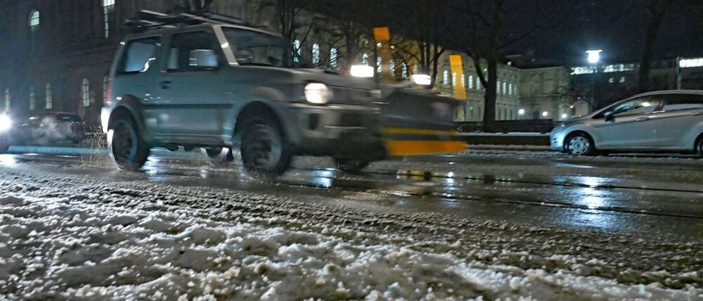09.01.2026, Bayern, München: Ein kleines SUV mit einer Schneeräumschaufel fährt an der alten Pinakothek vorbei. Im Vordergrund gefriert die Straße. Sturmtief «Elli» bringt heute viel Schnee und Eiseskälte in Teile Deutschlands. Mitunter besteht auch Glatteisgefahr durch überfrierenden Regen. Foto: Malin Wunderlich/dpa +++ dpa-Bildfunk +++