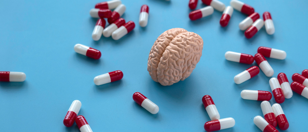 Eine Gehirnplastik, umgeben von Pillen, auf blauem Hintergrund (Illustration).