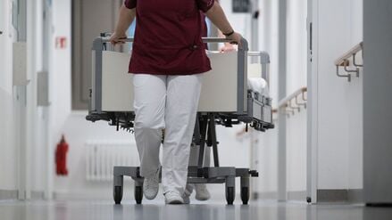 Eine Krankenpflegerin und ein Krankenpfleger schieben ein Krankenbett durch den Gang einer Station eines Krankenhauses (Symbolbild).