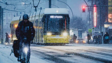 Eine Person mit Fahrrad auf einem mit Schnee bedecktem Radweg und eine Tram, aufgenommen waehrend starken Schneefalls in Berlin.
