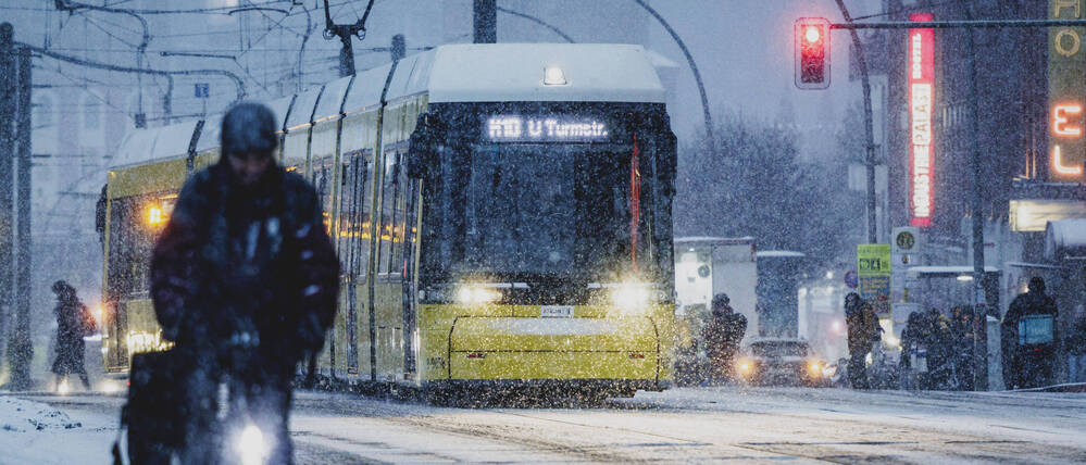 Eine Person mit Fahrrad auf einem mit Schnee bedecktem Radweg und eine Tram, aufgenommen waehrend starken Schneefalls in Berlin.