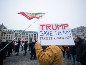 13.01.2026, Berlin: „Trump save Iran – Target Khamenei“, steht auf einem Schild während einer Demonstration zur Unterstützung der landesweiten Massenproteste gegen die Regierung im Iran auf dem Pariser Platz. Darüber hängt eine Fahne mit dem Bild von Reza Pahlavi, Sohn des letzten Schahs des Irans. 