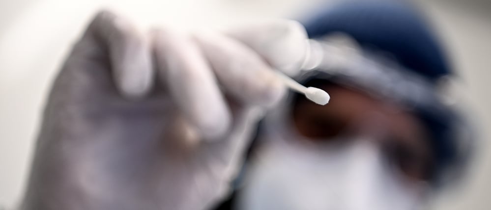 Ein Arzt hält ein Teststäbchen für die Entnahme einer Probe für einen PCR-Test beim Gesundheitsamt Neukölln in der Hand.