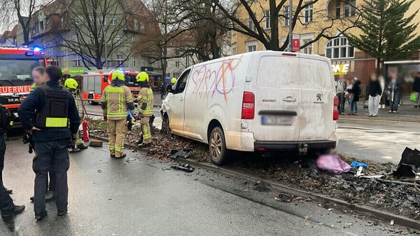 Ein weißer Transporter steht beschädigt auf einem Mittelstreifen, daneben Feuerwehrleute und Polizisten. 