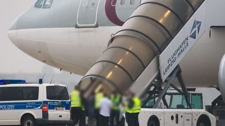 Menschen besteigen ein Flugzeug der Qatar Airways, vor dem Fahrzeuge der Bundespolizei stehen, auf dem Vorfeld am Flughafen Leipzig/Halle.