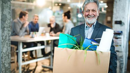 Happy mature businessman going to retirement and leaving the office while carrying his belongings and looking at camera.