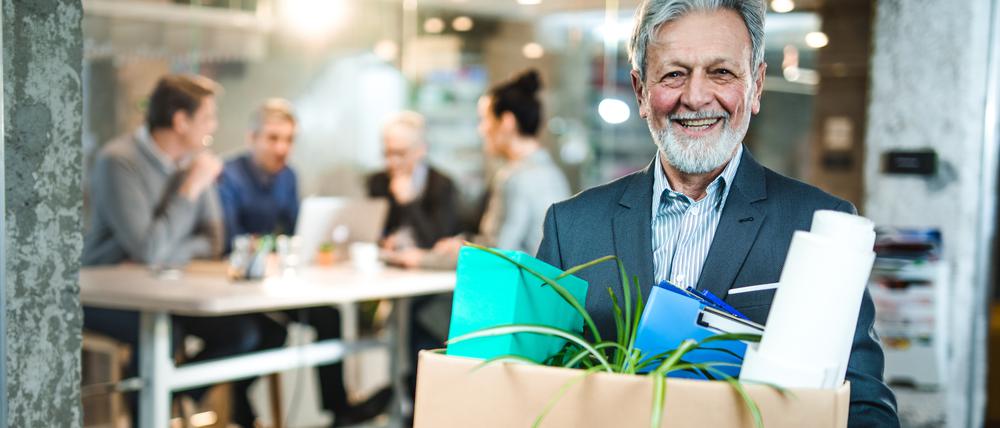 Happy mature businessman going to retirement and leaving the office while carrying his belongings and looking at camera.