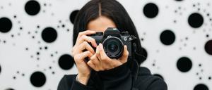 Unrecognizable young female photographer in stylish outfit standing near creative building and taking pictures on camera Copyright: xJordixSalasx