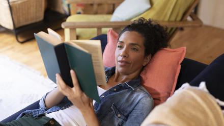 Frau liest ein Buch auf dem Sofa.