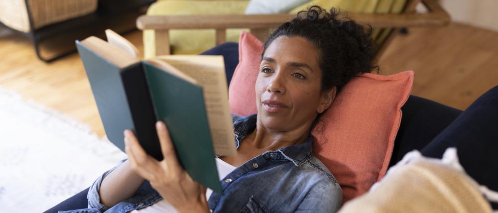 Frau liest ein Buch auf dem Sofa.