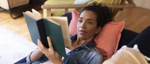 Frau liest ein Buch auf dem Sofa.