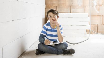 Thoughtful boy with book sitting on loft floor during renovation model released Symbolfoto property released HMEF01224 