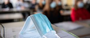 ARCHIV - 17.11.2020, Bayern, München: ILLUSTRATION - Eine Maske liegt im Unterricht auf Unterlagen, während im Hintergrund Schülerinnen und Schüler in einem Gymnasium mit Mund- und Nasenschutz zu sehen sind. (zu dpa «Große Mehrheit der Schüler sieht Lernrückstände durch Schließungen») Foto: Matthias Balk/dpa +++ dpa-Bildfunk +++