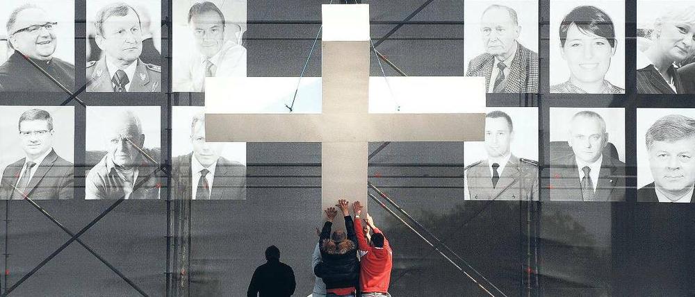 Gedenken. Vor Fotos der Absturzopfer wird in Warschau ein Kreuz aufgerichtet. Foto: AFP