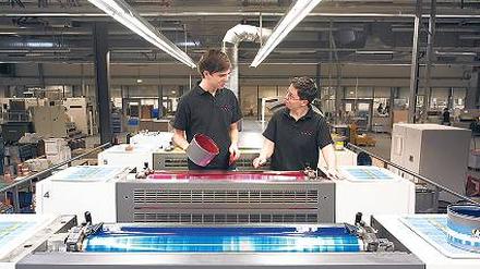 Teamwork. Zwei Drucker füllen die Farbe in einer Offset-Druckmaschine nach. Foto: dpa