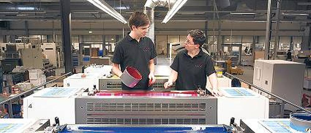 Teamwork. Zwei Drucker füllen die Farbe in einer Offset-Druckmaschine nach. Foto: dpa