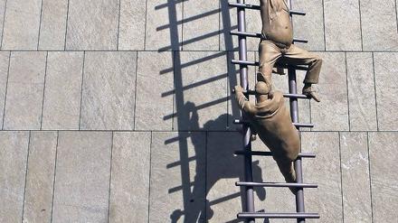 Karriereleiter. Ohne Top-Examen, am besten noch Auslandsaufenthalt oder Promotion braucht man sich gar nicht erst zu bewerben. Das Foto zeigt eine Skulptur des Bildhauers Peter Lenk an der Fassade einer Bank in Berlin. Foto: dpa