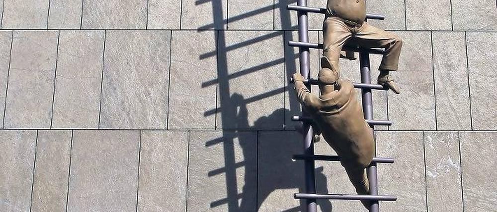 Karriereleiter. Ohne Top-Examen, am besten noch Auslandsaufenthalt oder Promotion braucht man sich gar nicht erst zu bewerben. Das Foto zeigt eine Skulptur des Bildhauers Peter Lenk an der Fassade einer Bank in Berlin. Foto: dpa