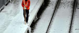 Ein S-Bahn-Mitarbeiter fegt am Dienstag Schnee vom Bahnsteig des S-Bahnhofs Ostkreuz. In der Nacht zu Mittwoch hat es erneut geschneit.