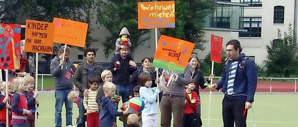 Mit Plakaten und Trillerpfeifen demonstrieren Eltern und Kinder auf dem Platz an der Körtestraße, im Hintergrund die Wohnhäuser.
