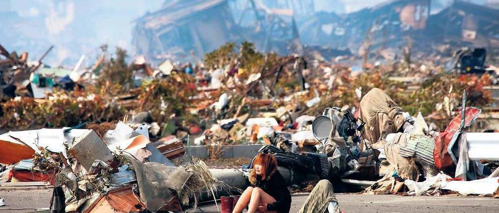 Einsam inmitten der Verwüstung. Eine weinende Frau sitzt zwischen den Trümmern ihrer von dem Tsunami zerstörten Stadt Natori im Norden des Landes. Fotos: Reuters(1), AFP(2)