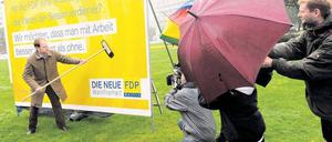 Nass gemacht. FDP-Chef Christoph Meyer klebt – im  Regen stehend und umtost von Autokarawanen am Ernst-Reuter-Platz – die ersten Plakate. Foto: dpa/Gambarini
