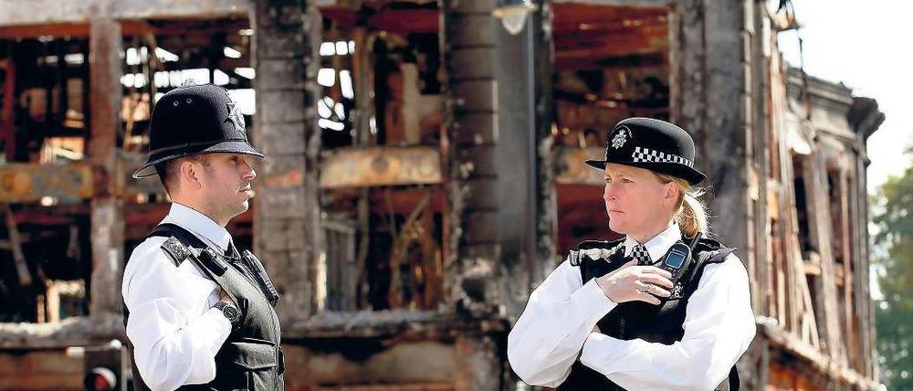 Quer durch London. Polizisten sichern ein ausgebranntes Gebäude im Nordlondoner Viertel Tottenham. Schäden nach Randale gab es auch in Brixton südlich der Themse. Fotos: dpa