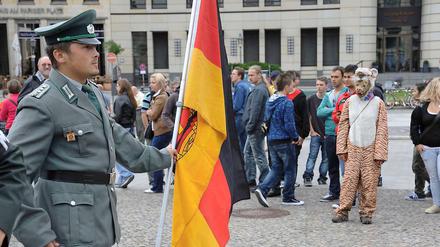 Mann mit DDR-Uniform und Fahne am Brandenburger Tor.